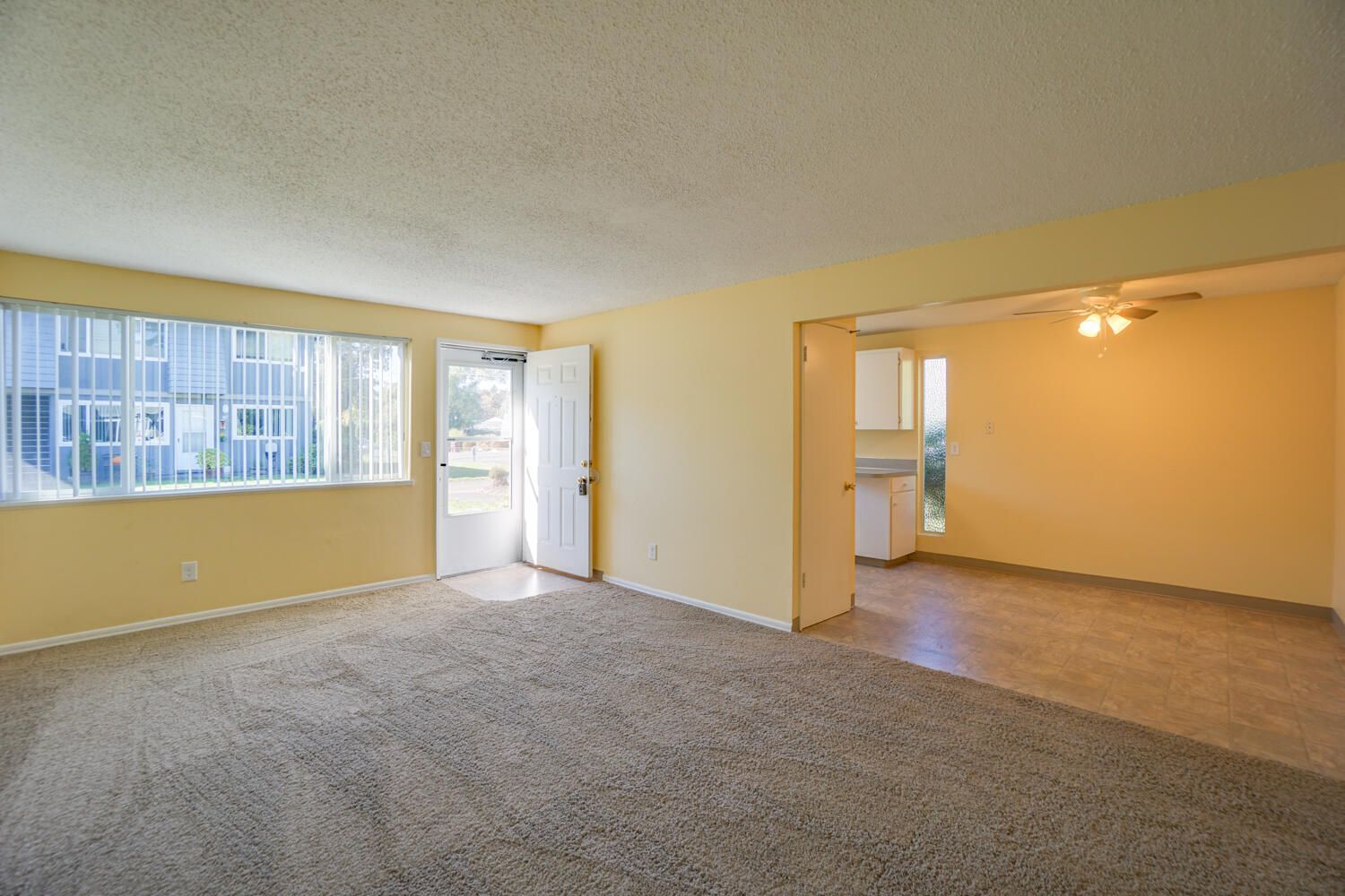An empty living room with a large window and a carpeted floor.