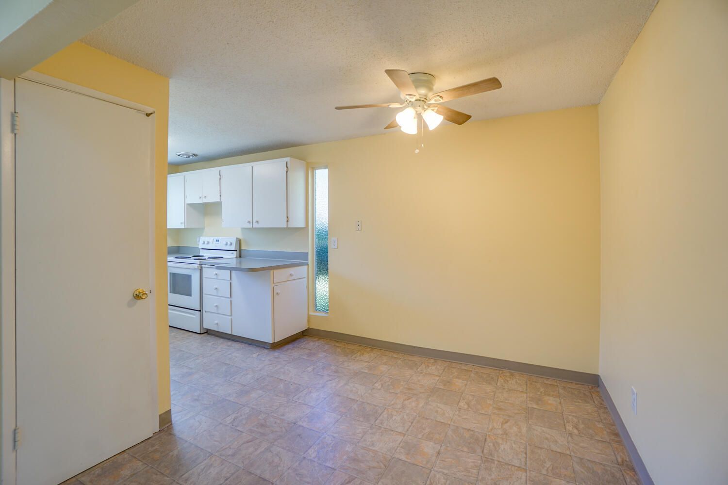 An empty room with a ceiling fan and a kitchen in the background.