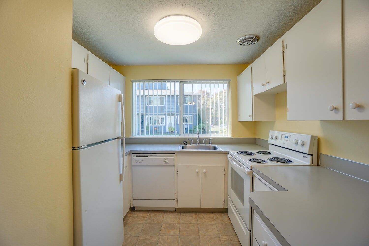 A kitchen with white cabinets , a stove , a refrigerator , and a window.