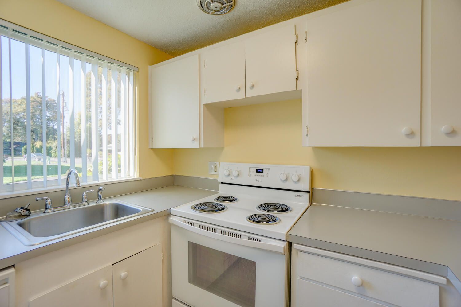 A kitchen with a stove , sink , dishwasher and window.