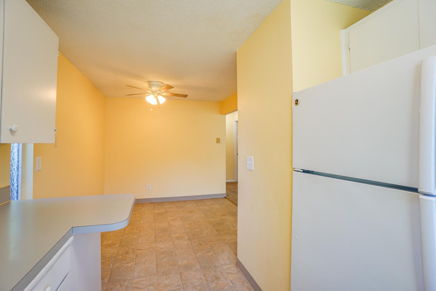 An empty kitchen with a refrigerator and a ceiling fan.