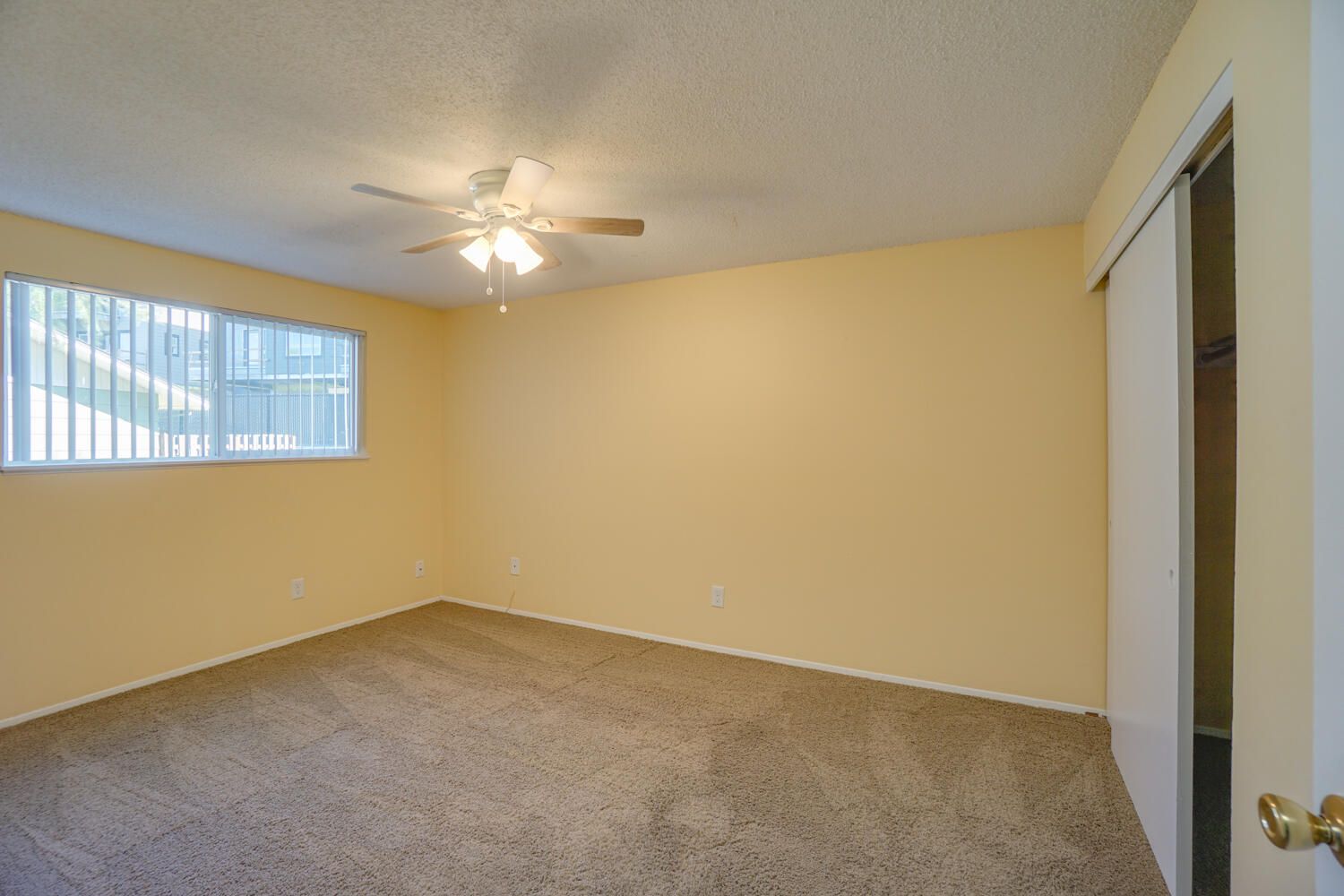 An empty bedroom with a ceiling fan and a window.