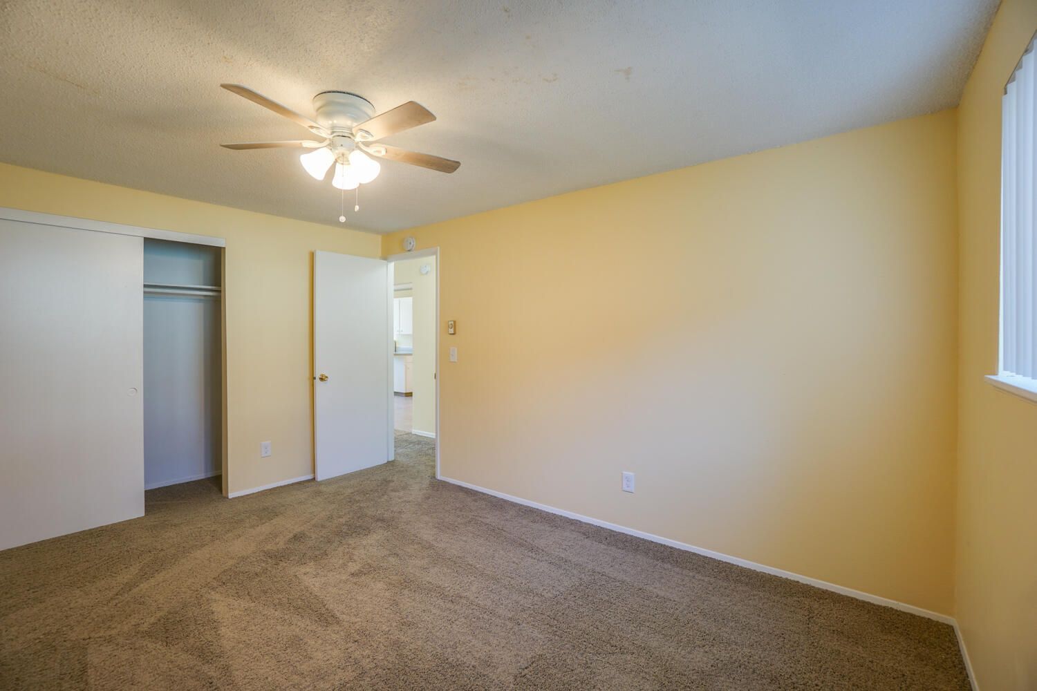 An empty bedroom with a ceiling fan and a window.