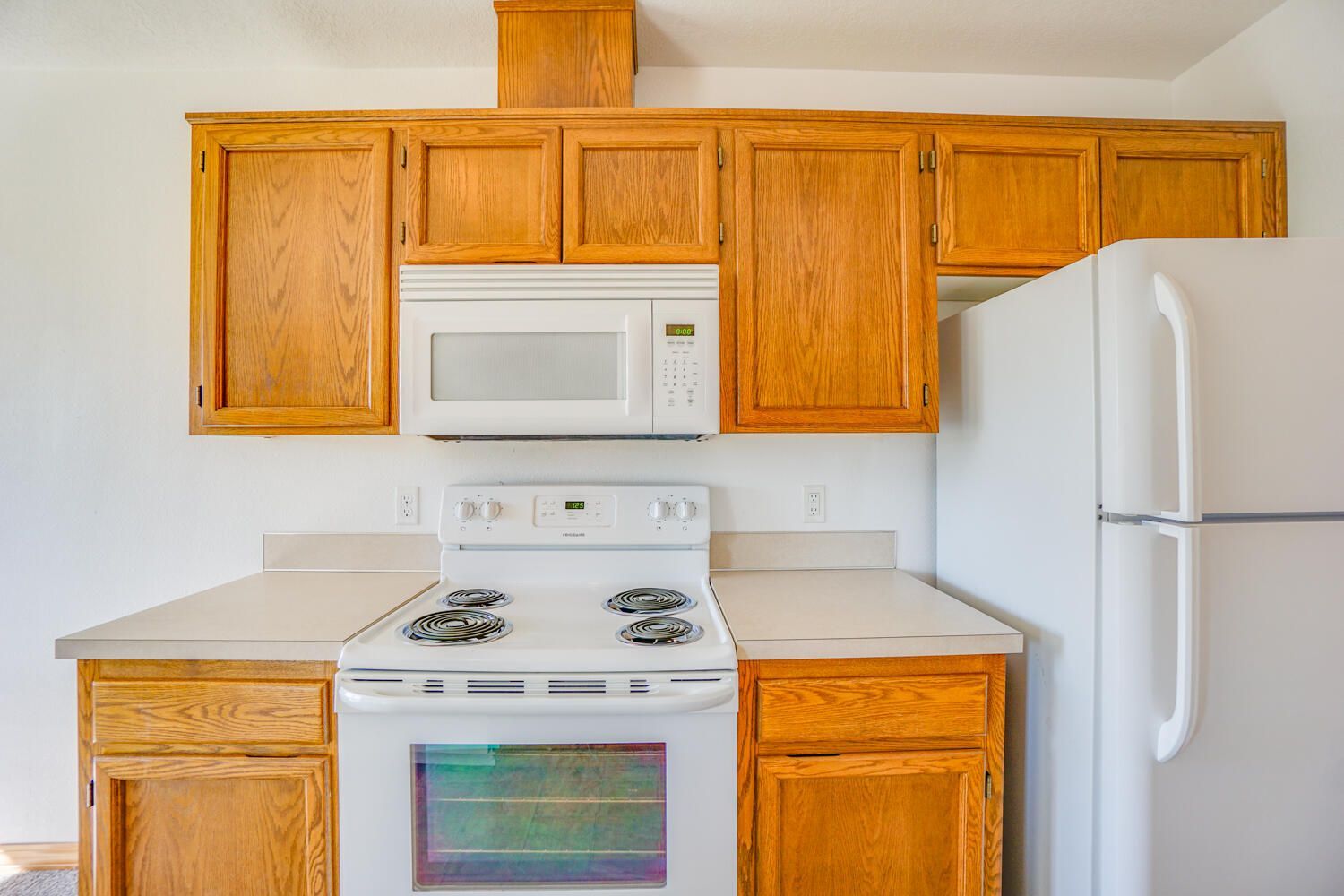 A kitchen with a stove , microwave , refrigerator and wooden cabinets.