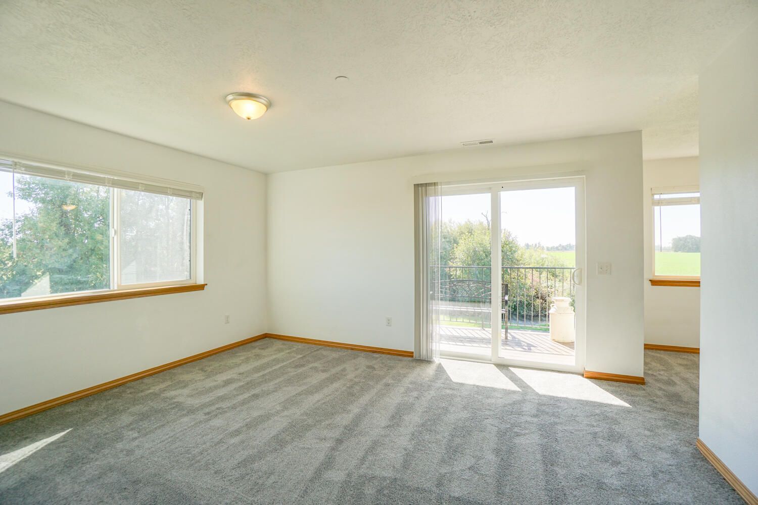 An empty living room with a sliding glass door and two windows.