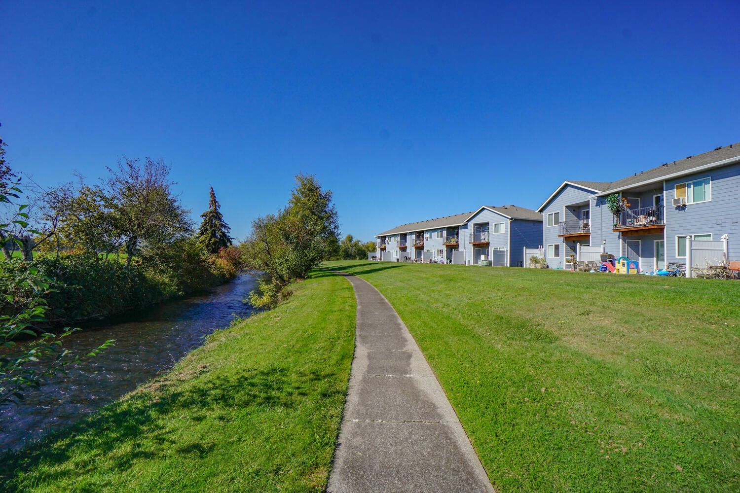 A path leading to a river with buildings in the background.