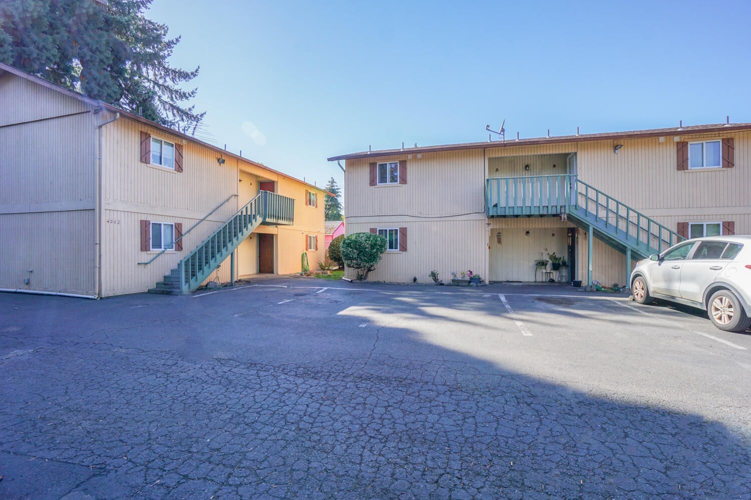 A parking lot in front of a building with stairs leading up to the second floor.