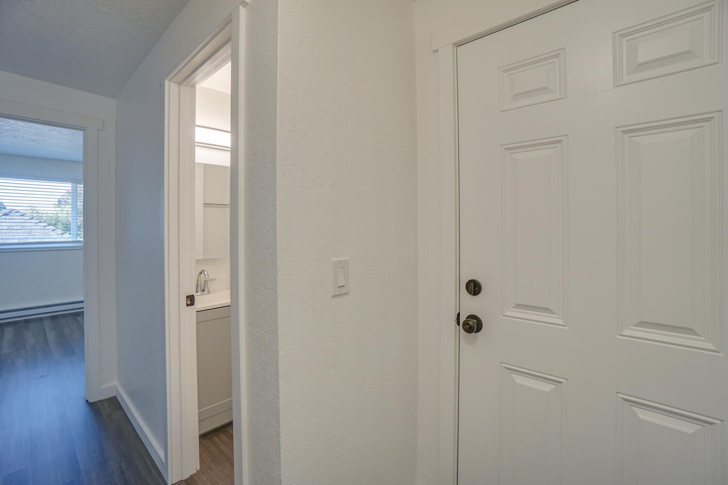 A hallway with a white door and a bathroom in the background.