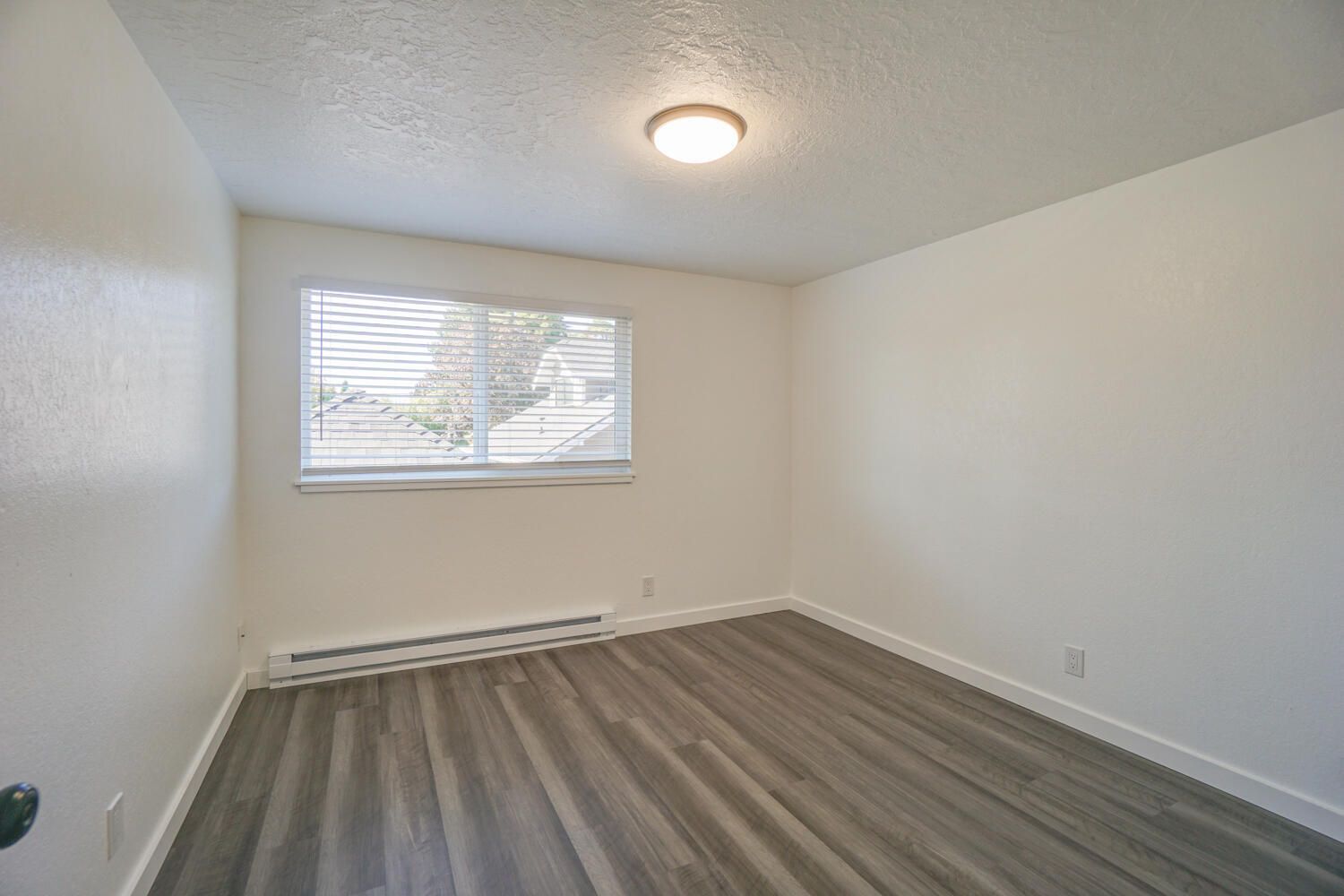 An empty bedroom with hardwood floors and a window.