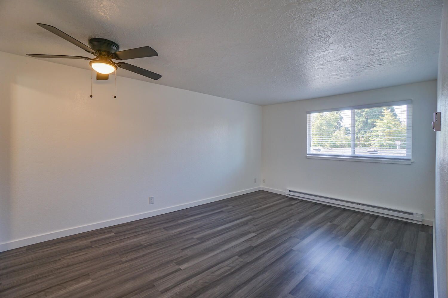 An empty living room with a ceiling fan and a window.