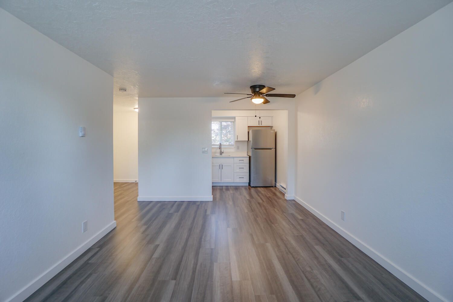 An empty living room with hardwood floors and a ceiling fan.