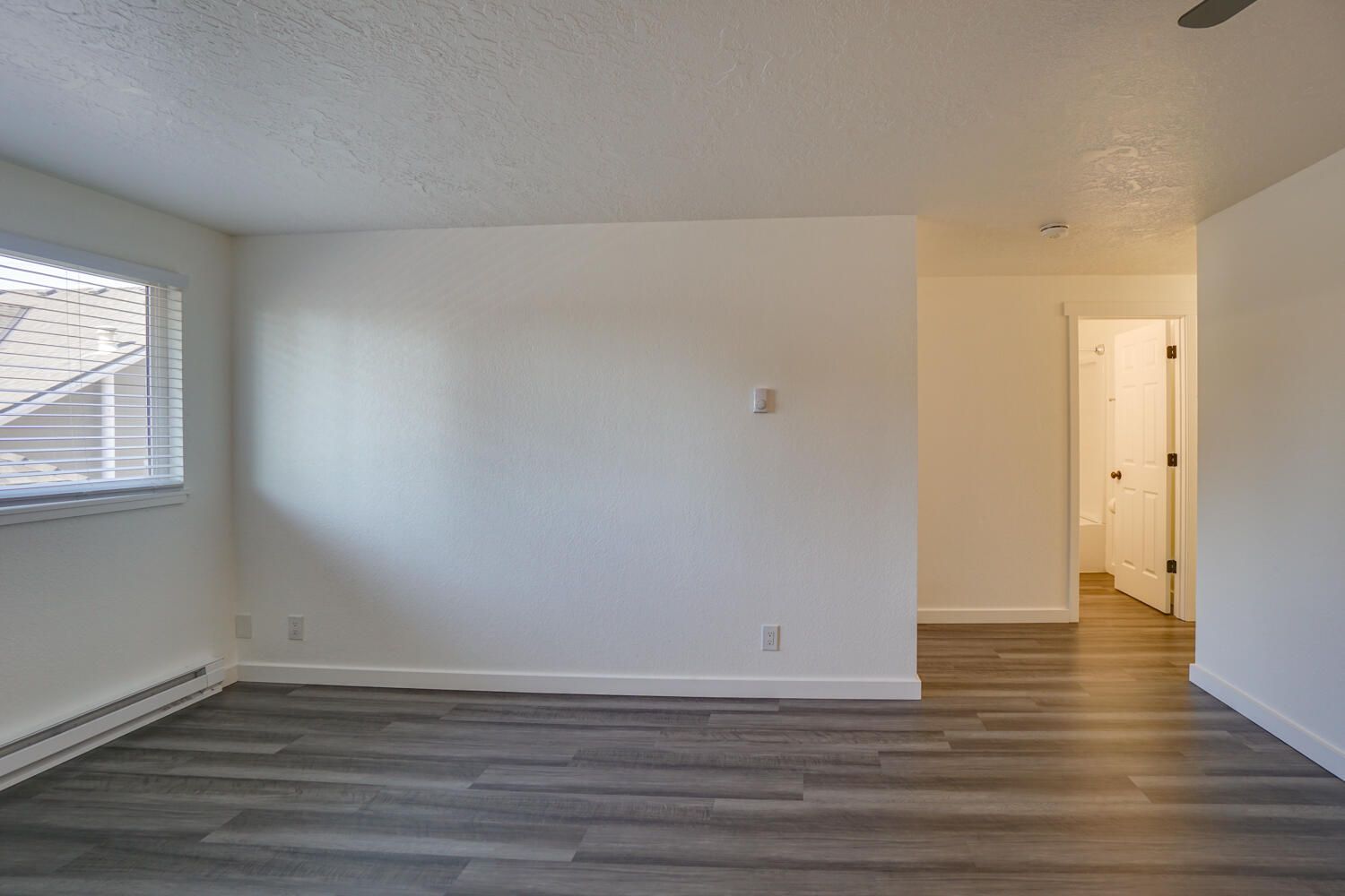 An empty living room with hardwood floors and white walls.