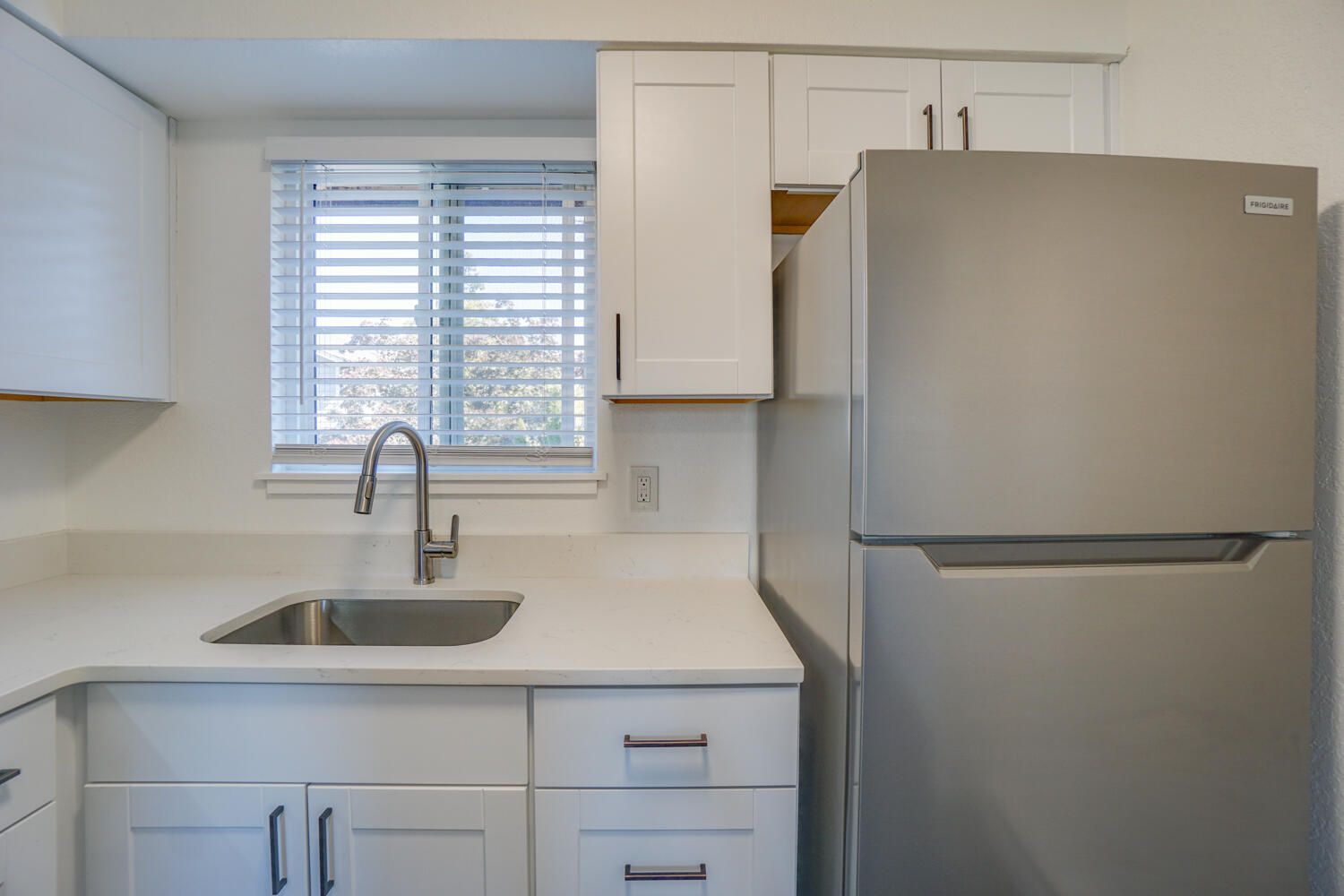A kitchen with a sink , refrigerator , and window.