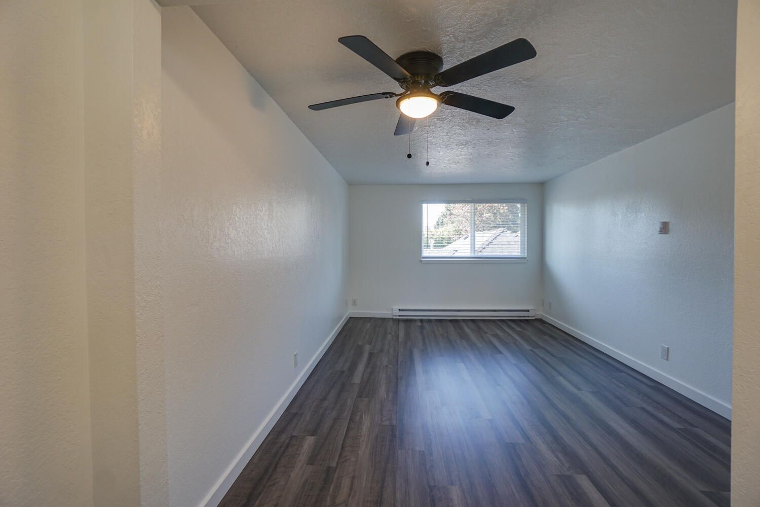 An empty room with a ceiling fan and a window.