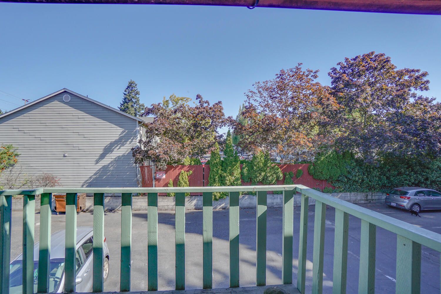 A balcony with a green railing overlooking a parking lot and a house.