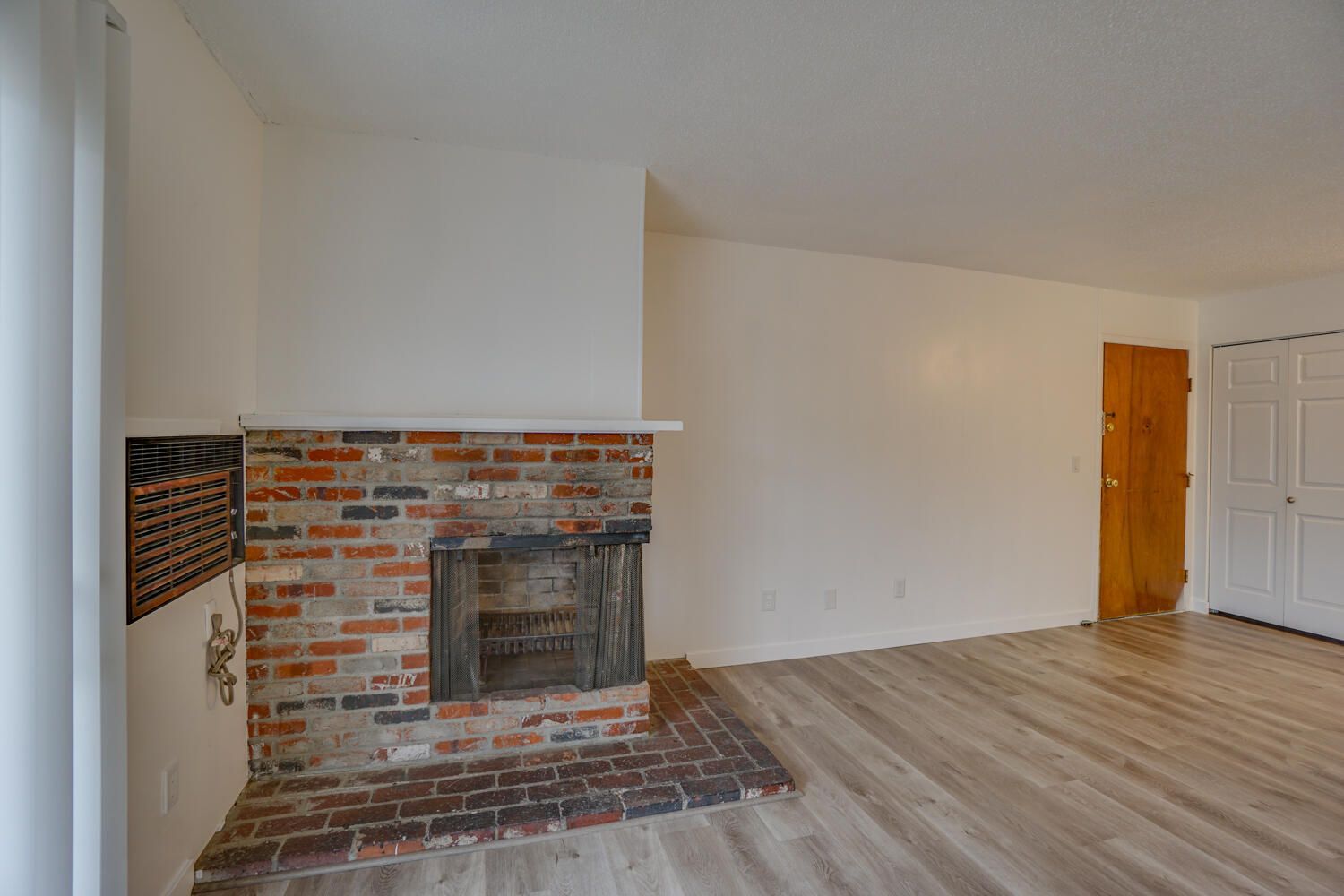 An empty living room with a brick fireplace and hardwood floors.