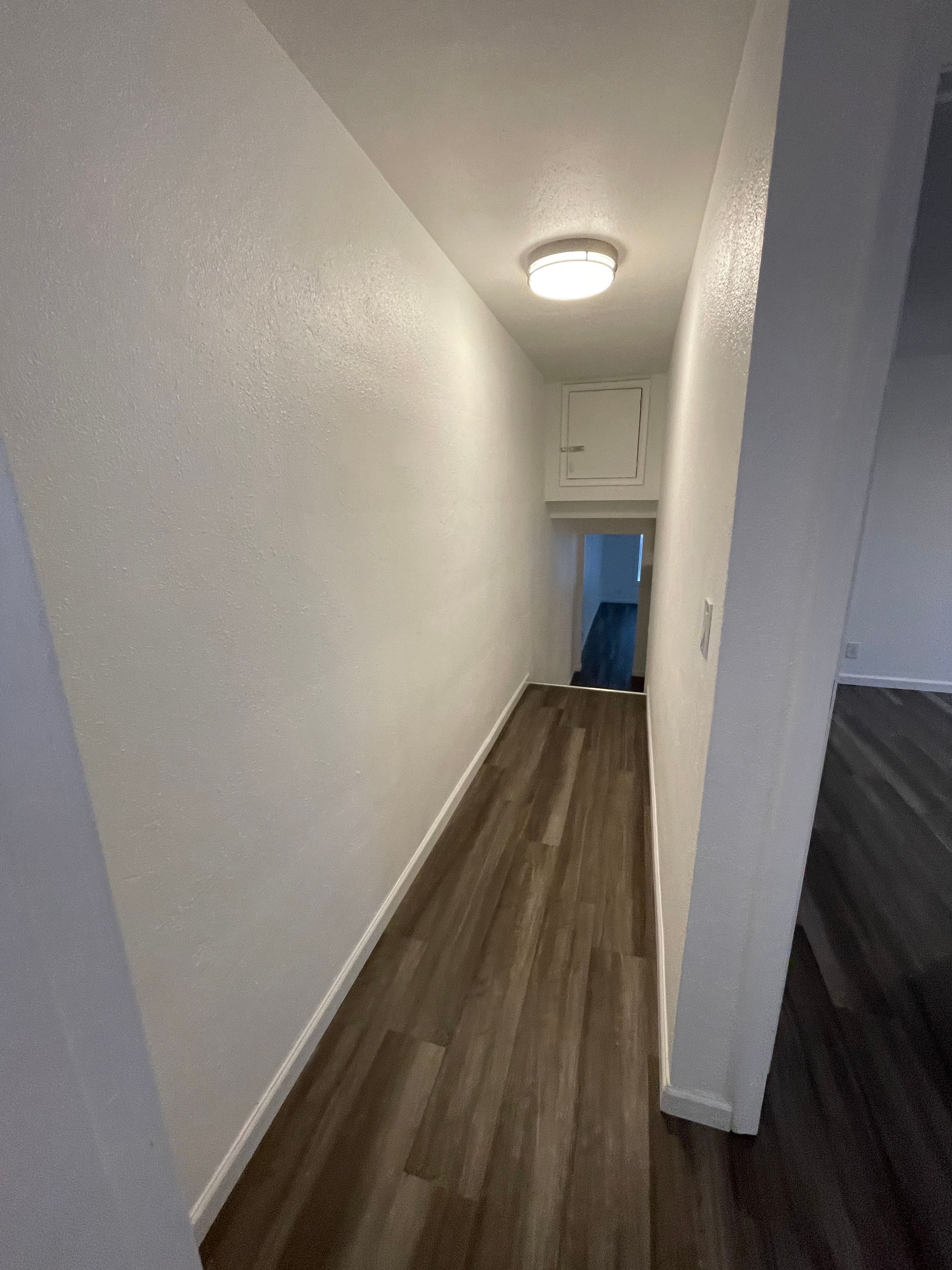 A long hallway with hardwood floors and white walls in a house.