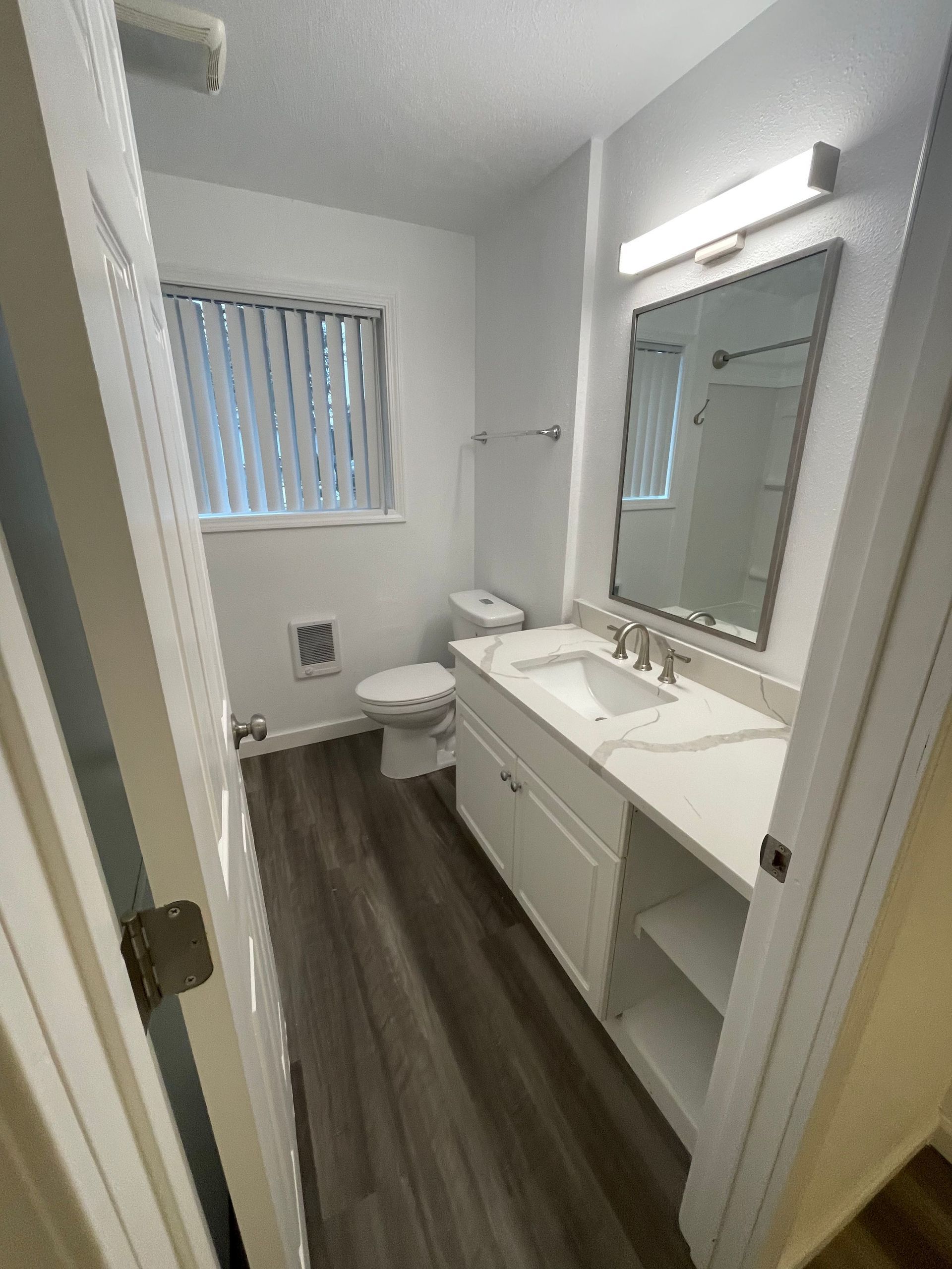 A bathroom with a toilet , sink , mirror and window.