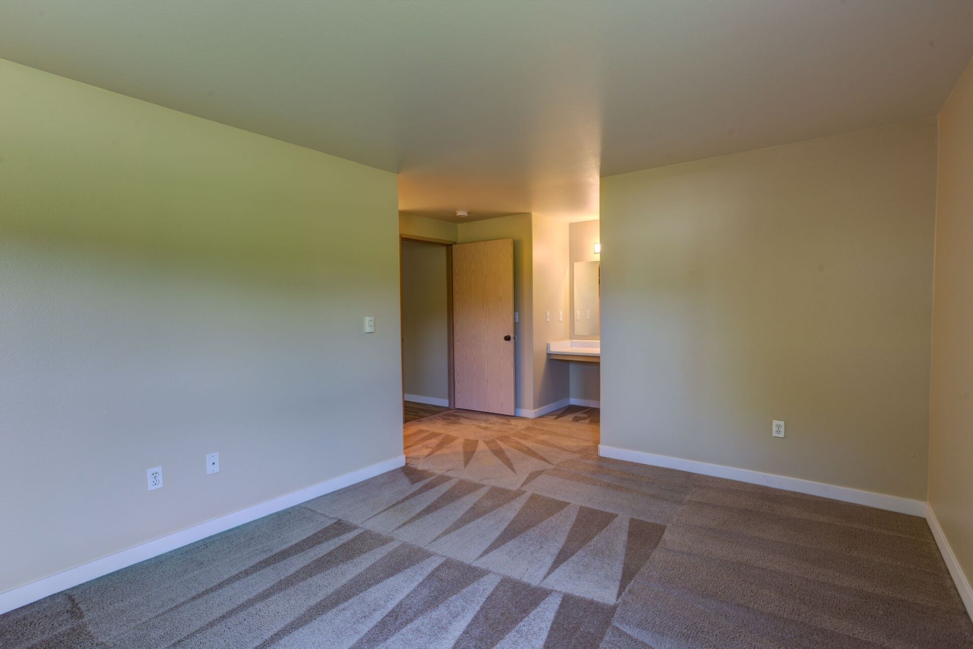 An empty bedroom with a carpeted floor and a bathroom.