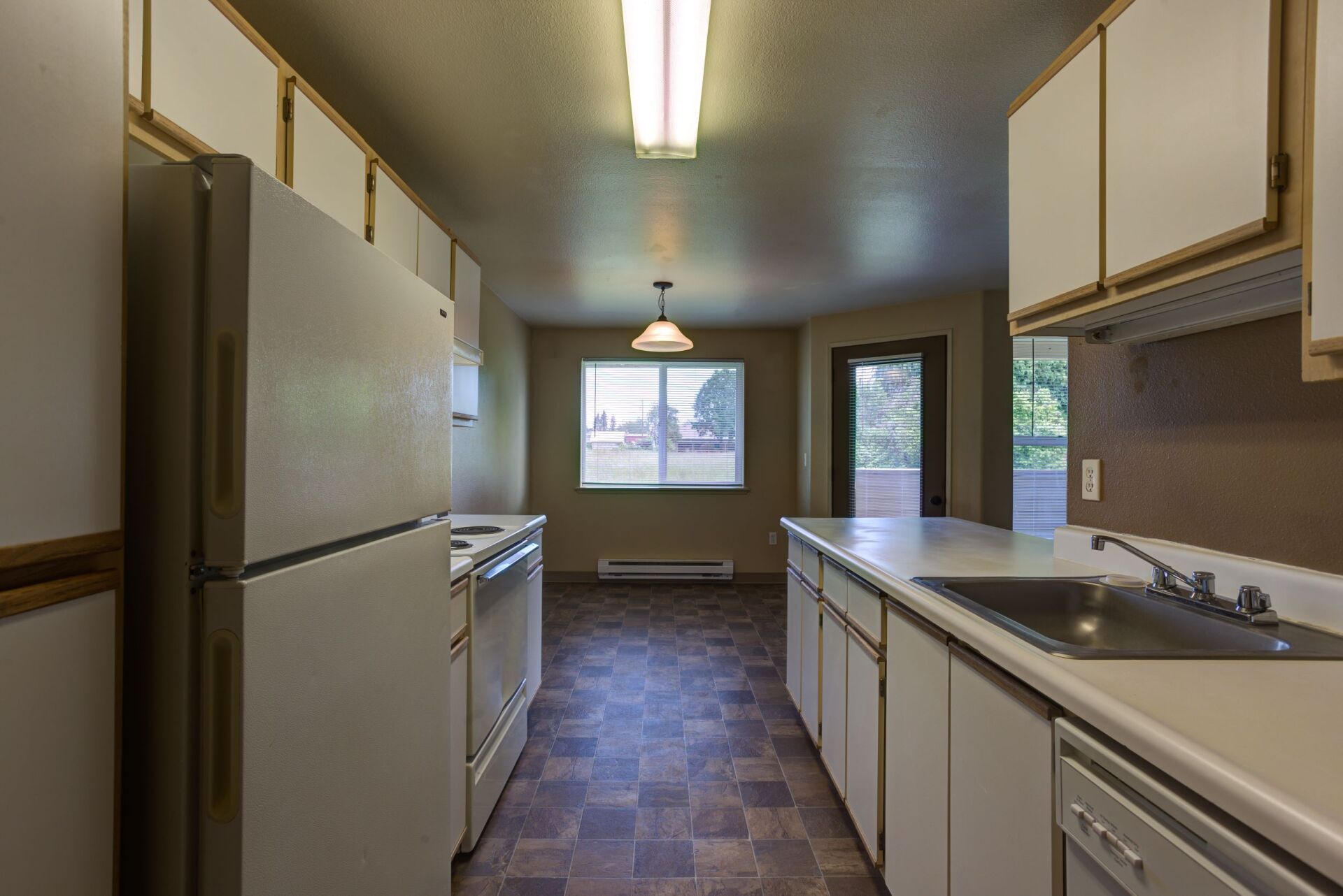 An empty kitchen with white cabinets and a refrigerator