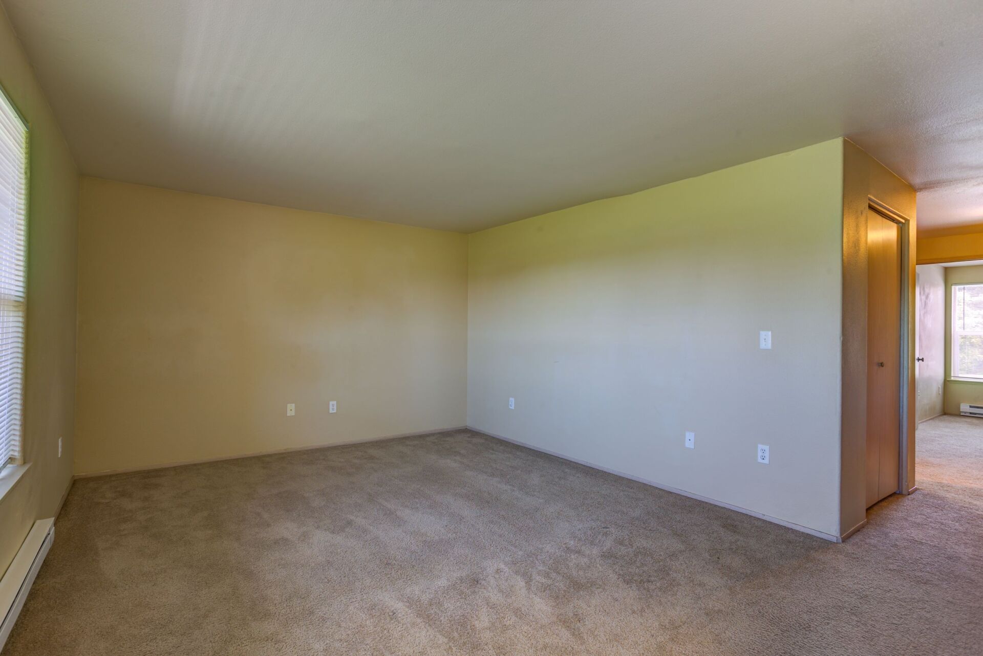 An empty living room with a carpeted floor and a window.