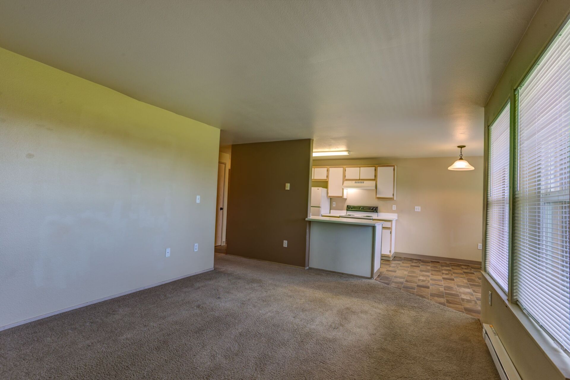 An empty living room with a kitchen in the background.