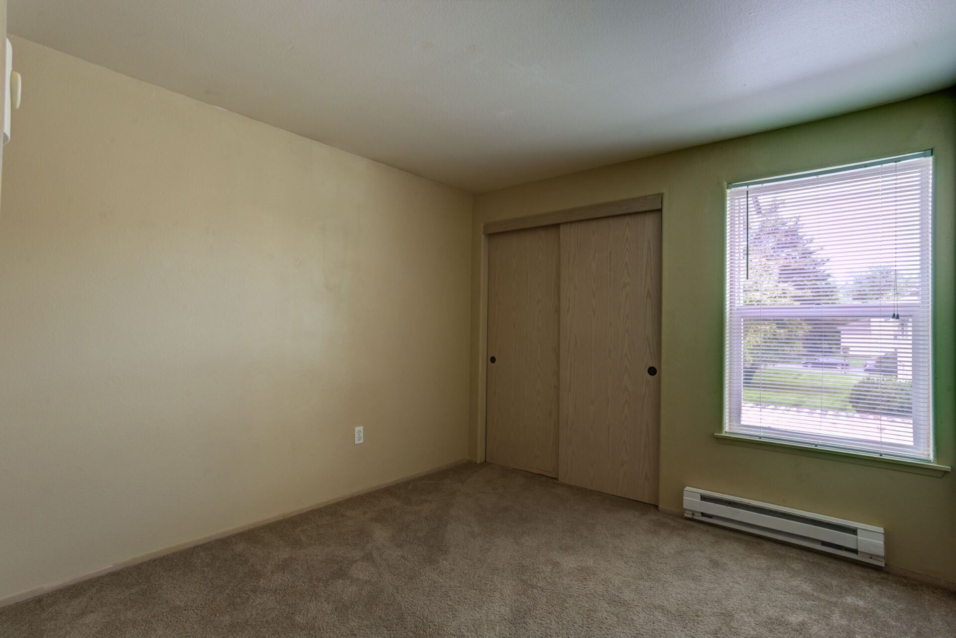 An empty bedroom with a window and a closet.