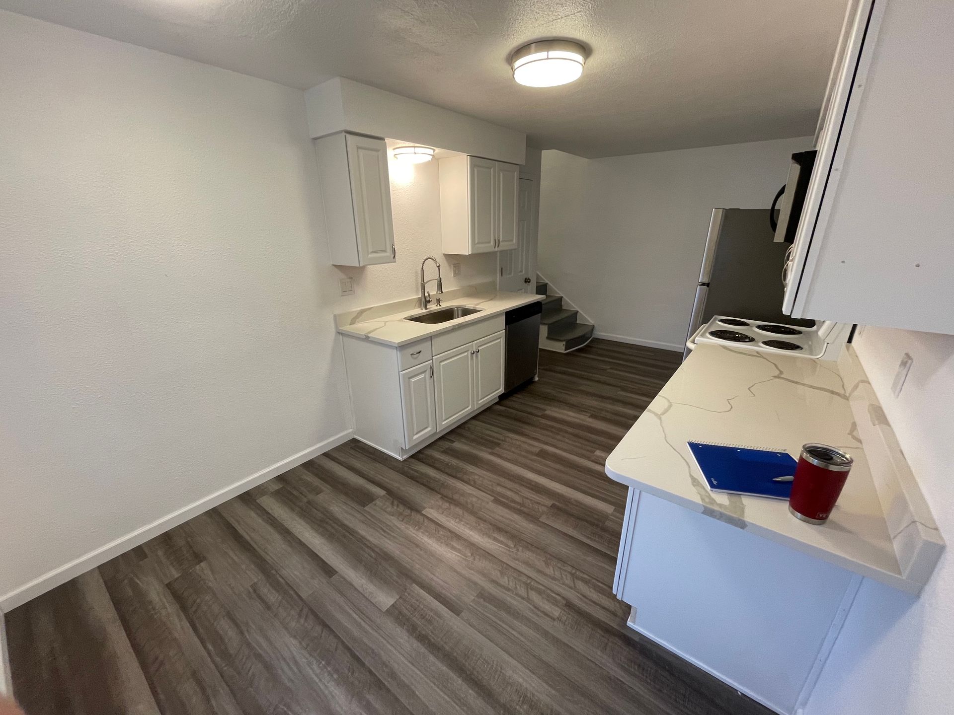 A kitchen with white cabinets , a sink , a stove , and a refrigerator.