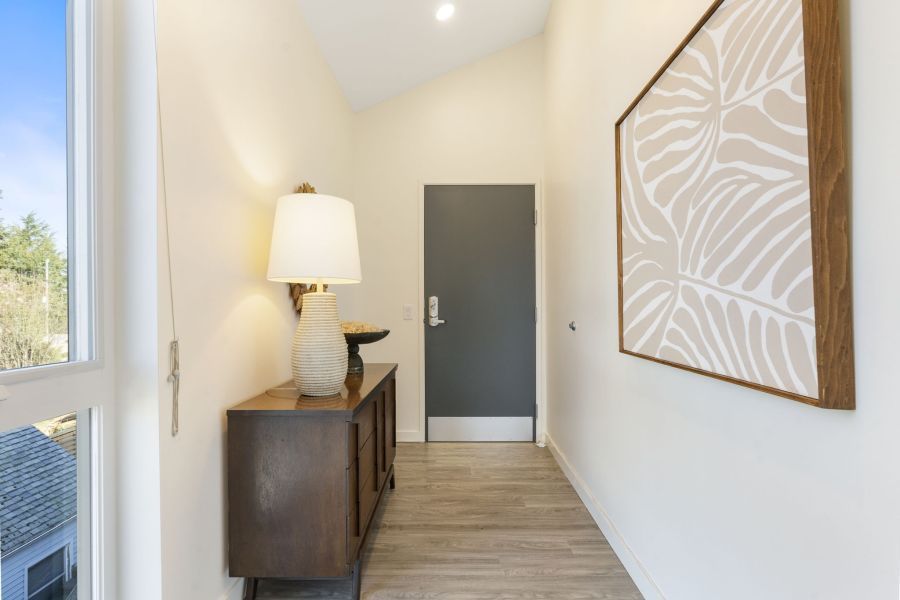 A hallway with a dresser , lamp , picture on the wall and a door.