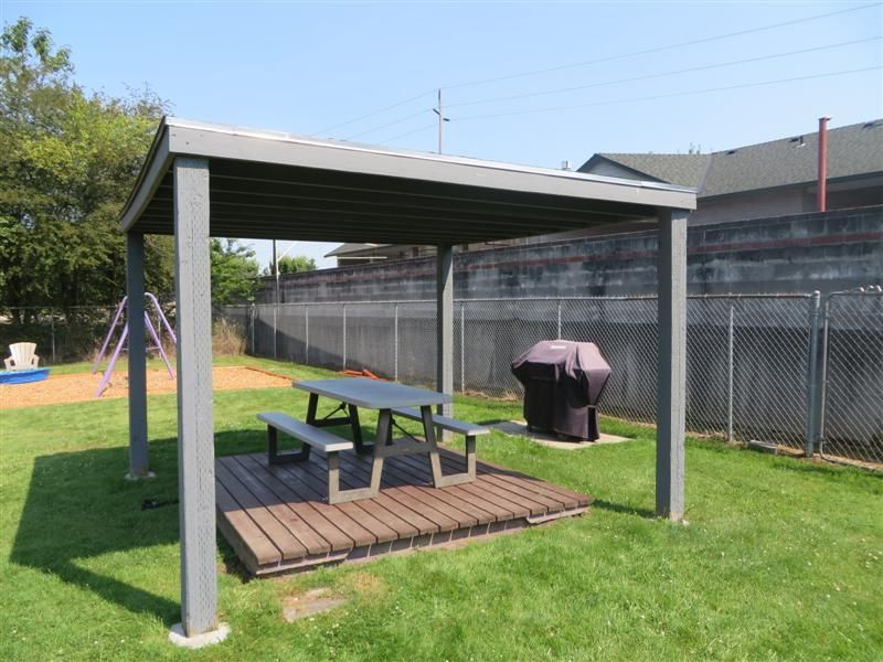 A picnic table and grill under a pergola in a park.