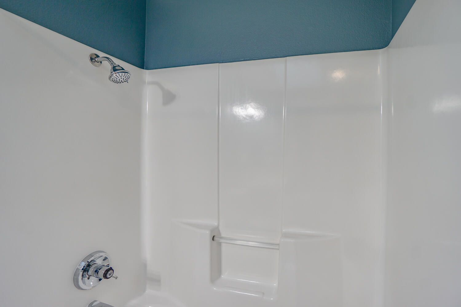 White shower stall with chrome fixtures against blue wall.
