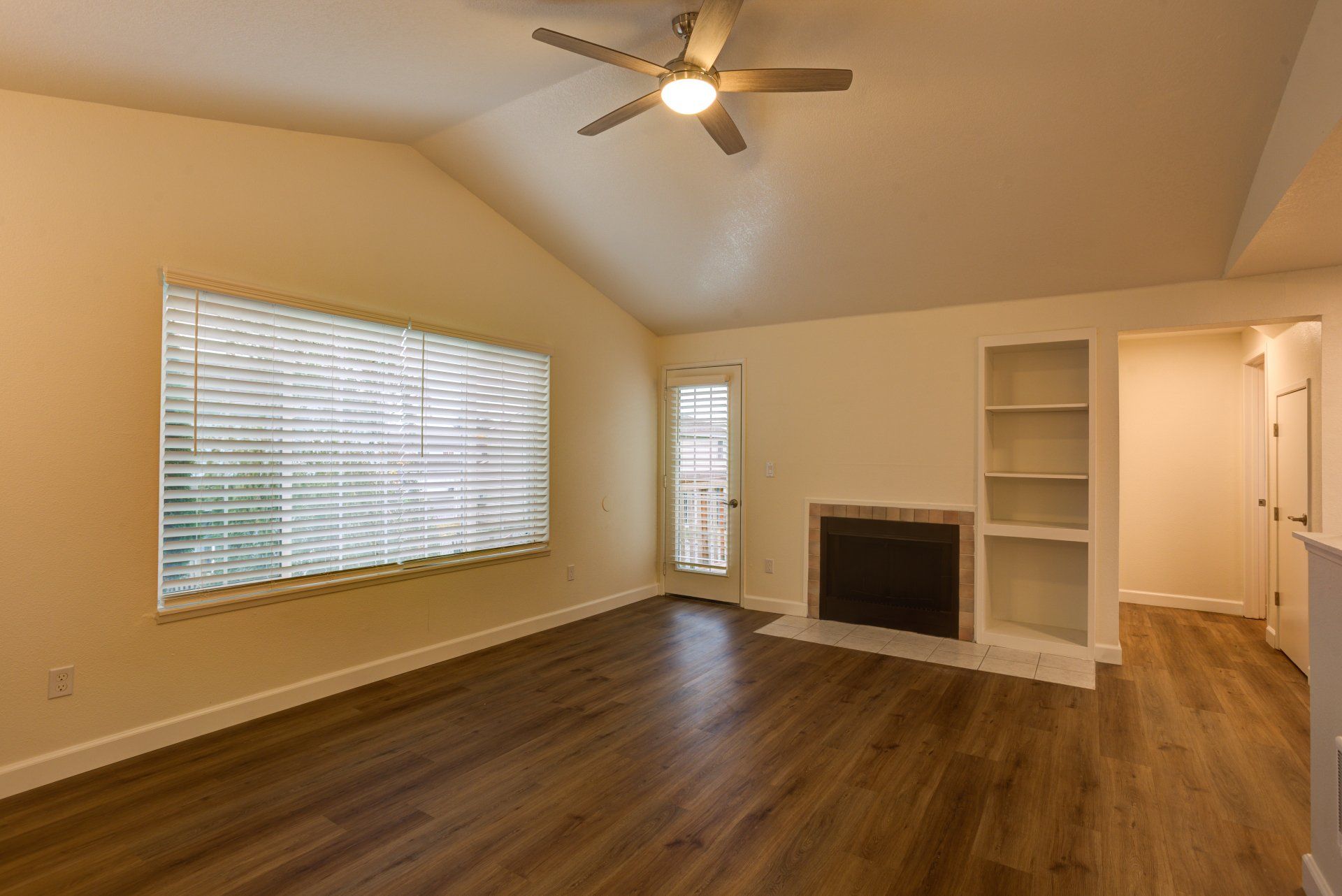 An empty living room with a fireplace and a ceiling fan.