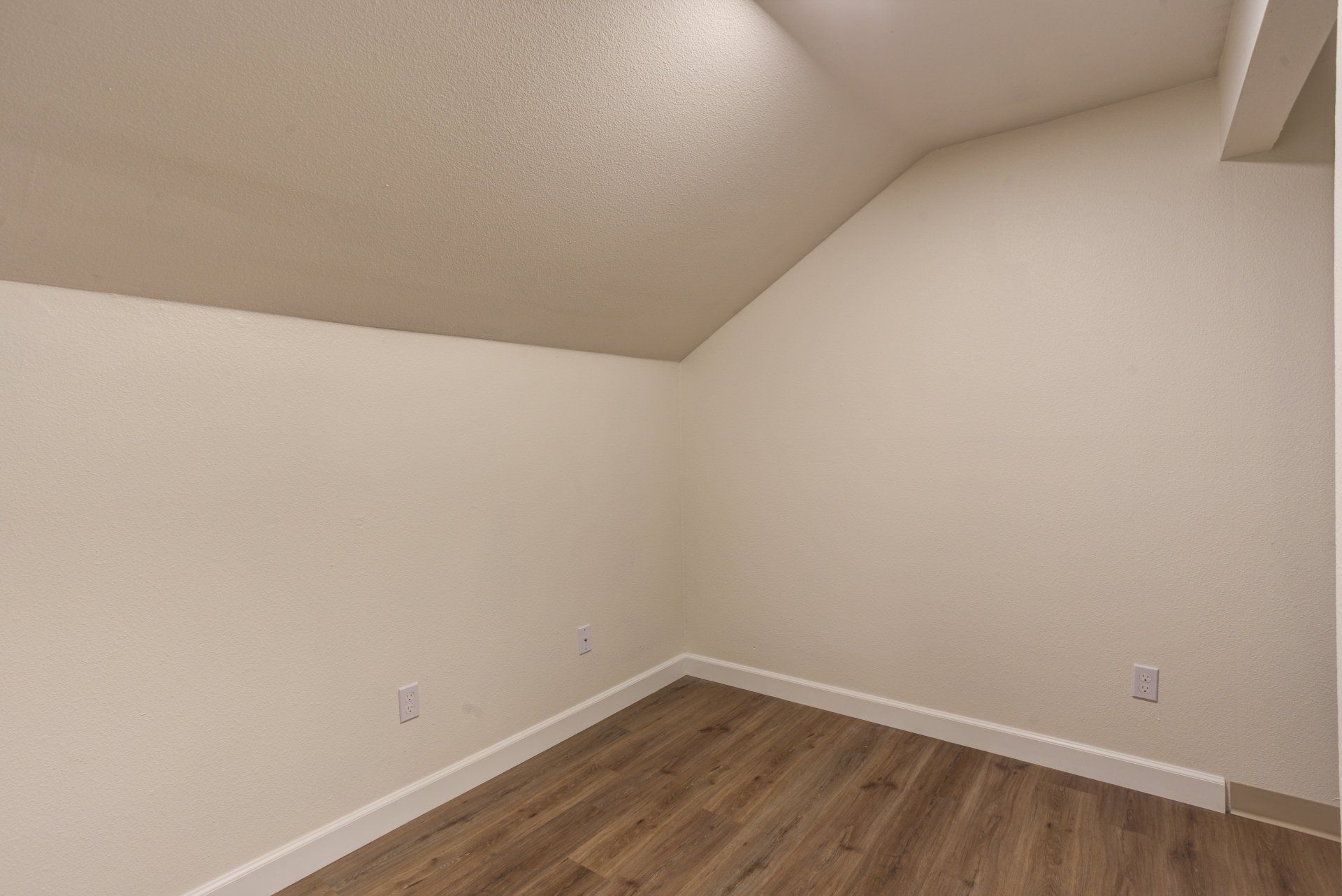 An empty room with a vaulted ceiling and hardwood floors.