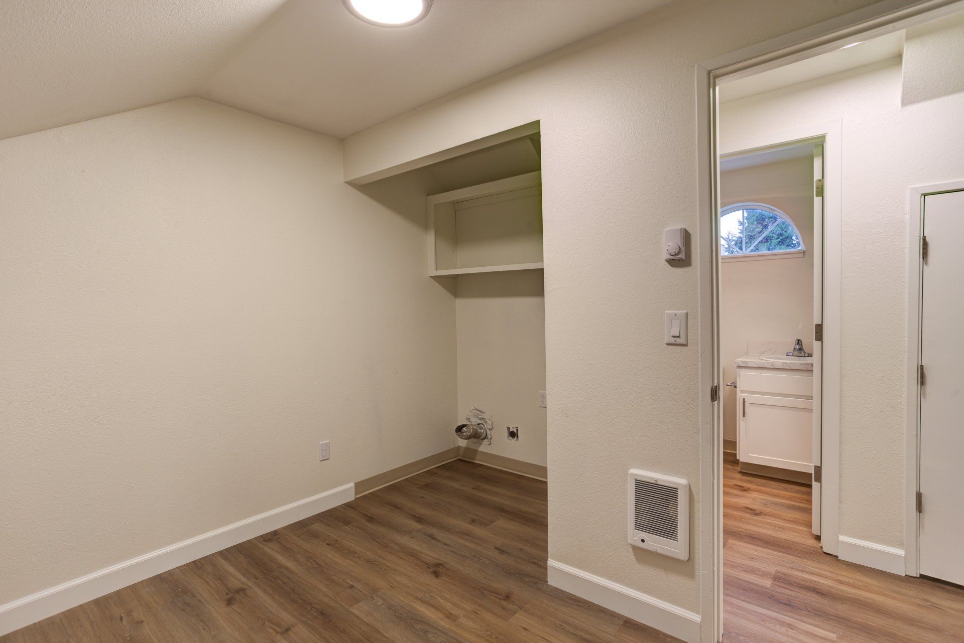 An empty room with hardwood floors and a doorway leading to a bathroom.