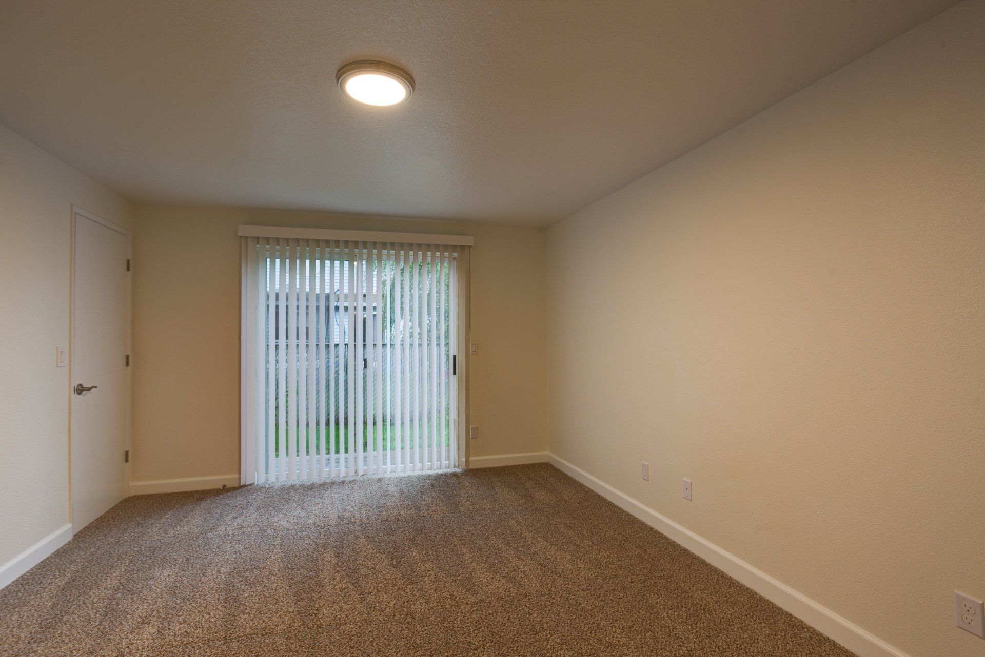 An empty living room with a sliding glass door and blinds.