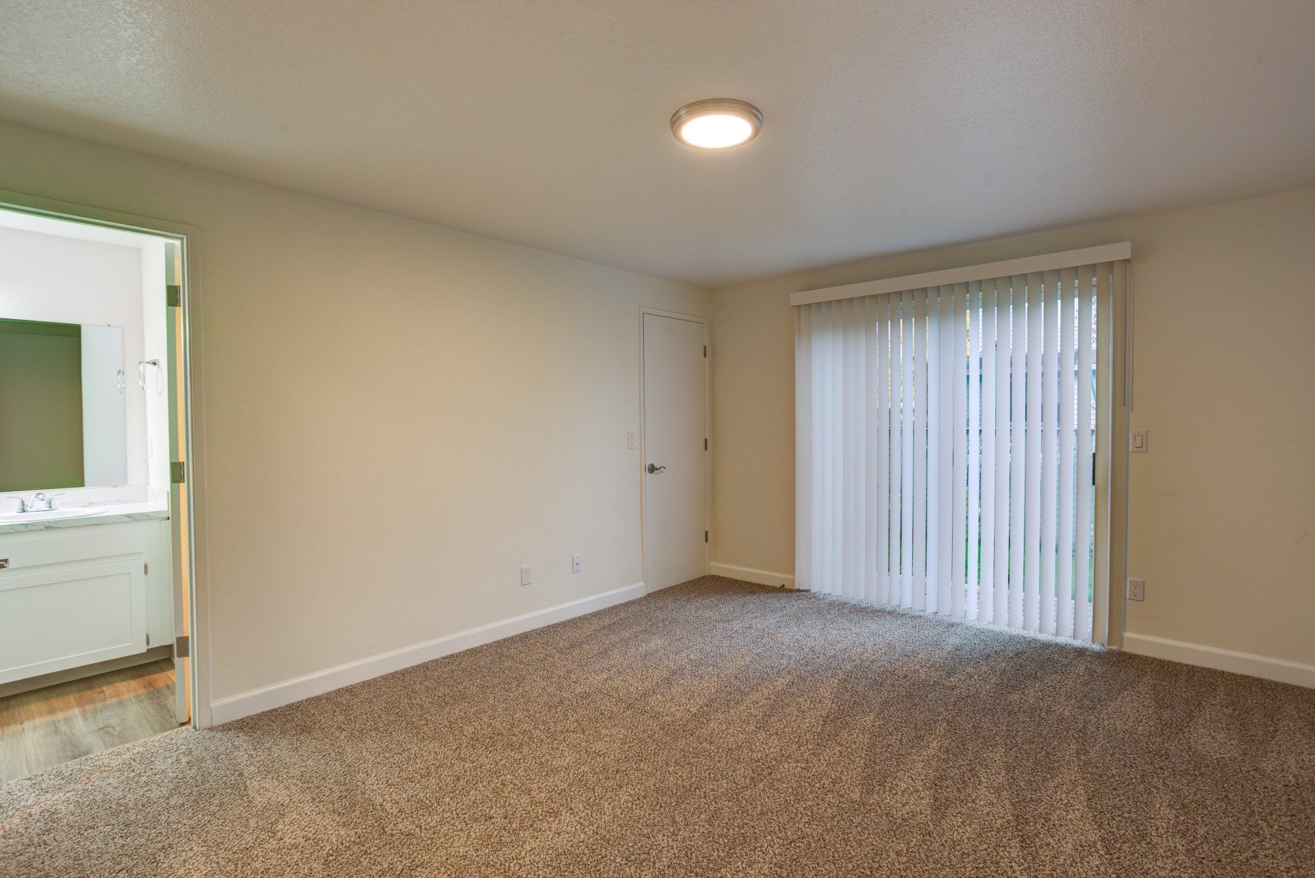 An empty living room with a sliding glass door and blinds.