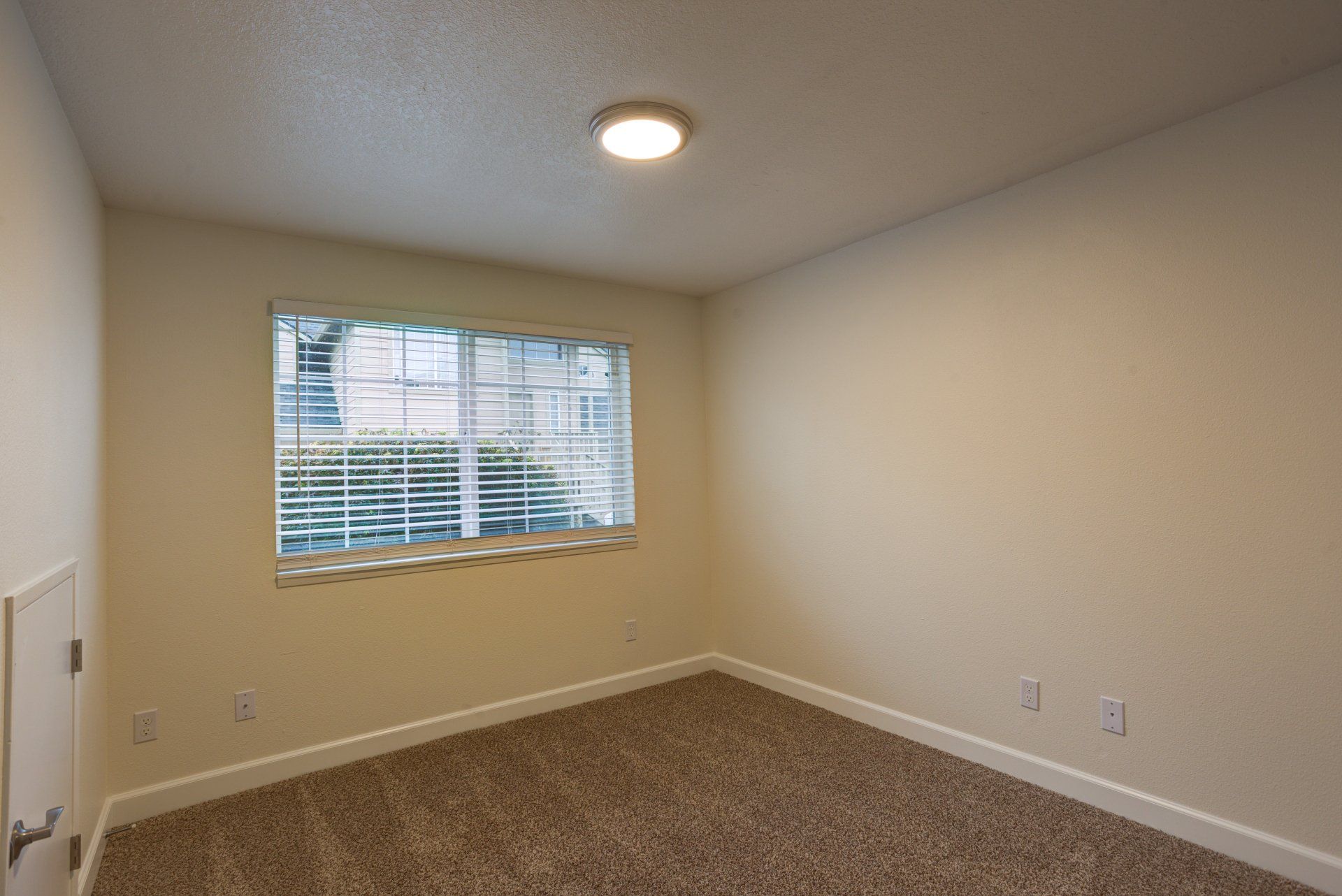 An empty bedroom with a window and a light on the ceiling.