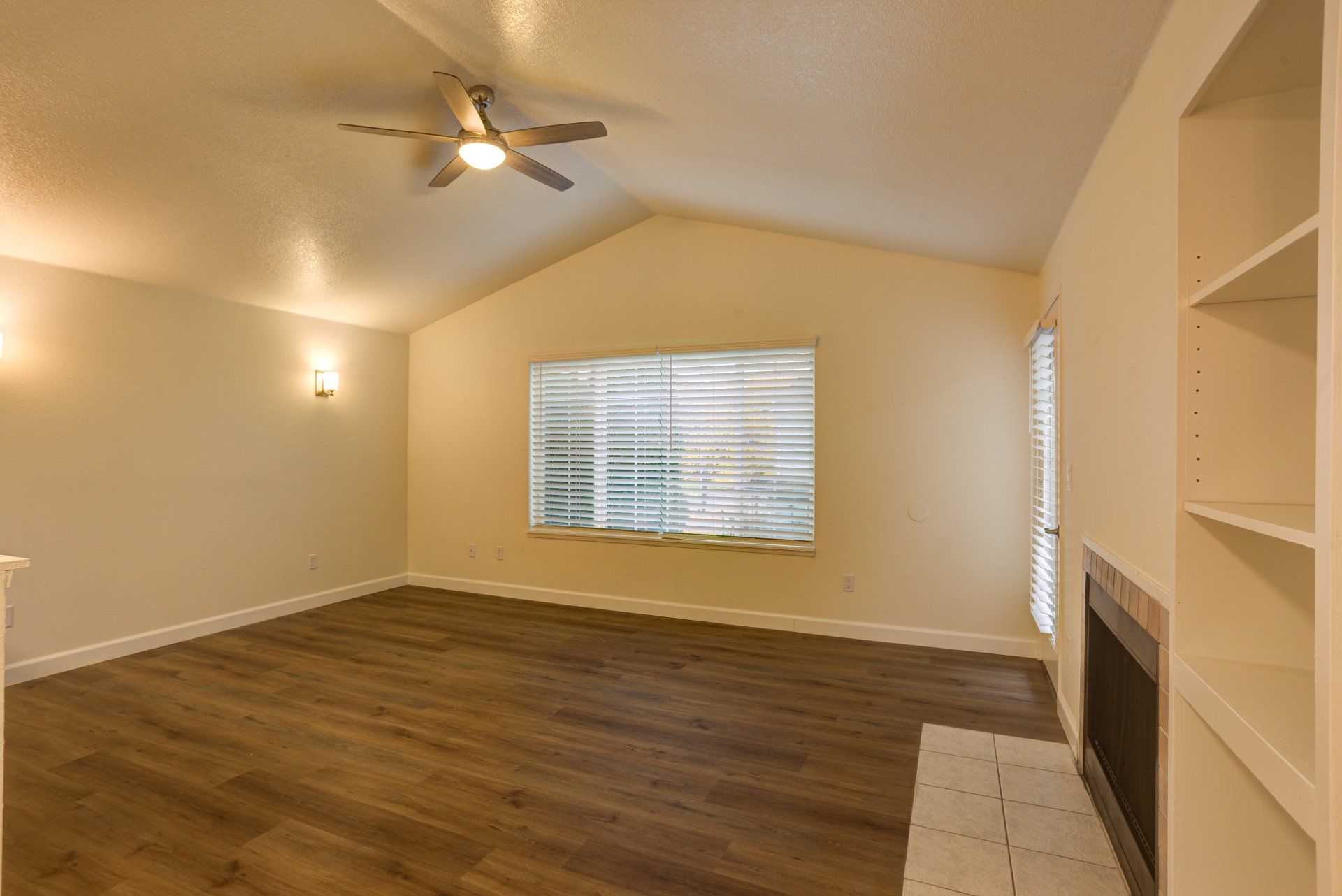 An empty living room with hardwood floors , a fireplace and a ceiling fan.