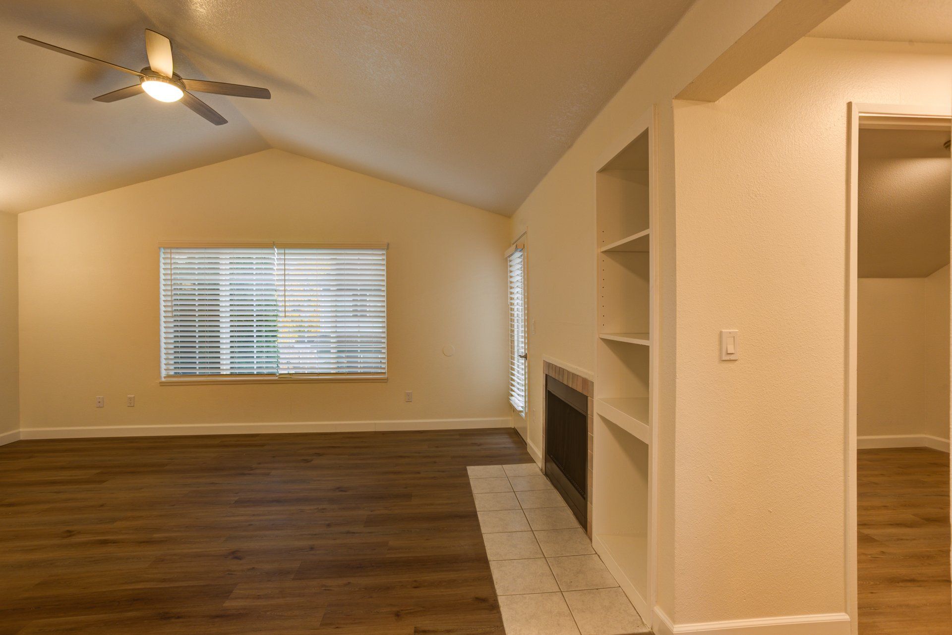 An empty living room with a fireplace and a ceiling fan.
