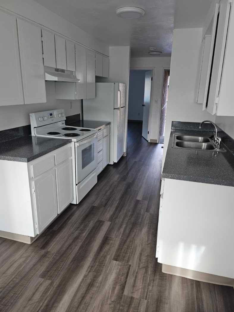 A kitchen with a stove , refrigerator , sink and cabinets.