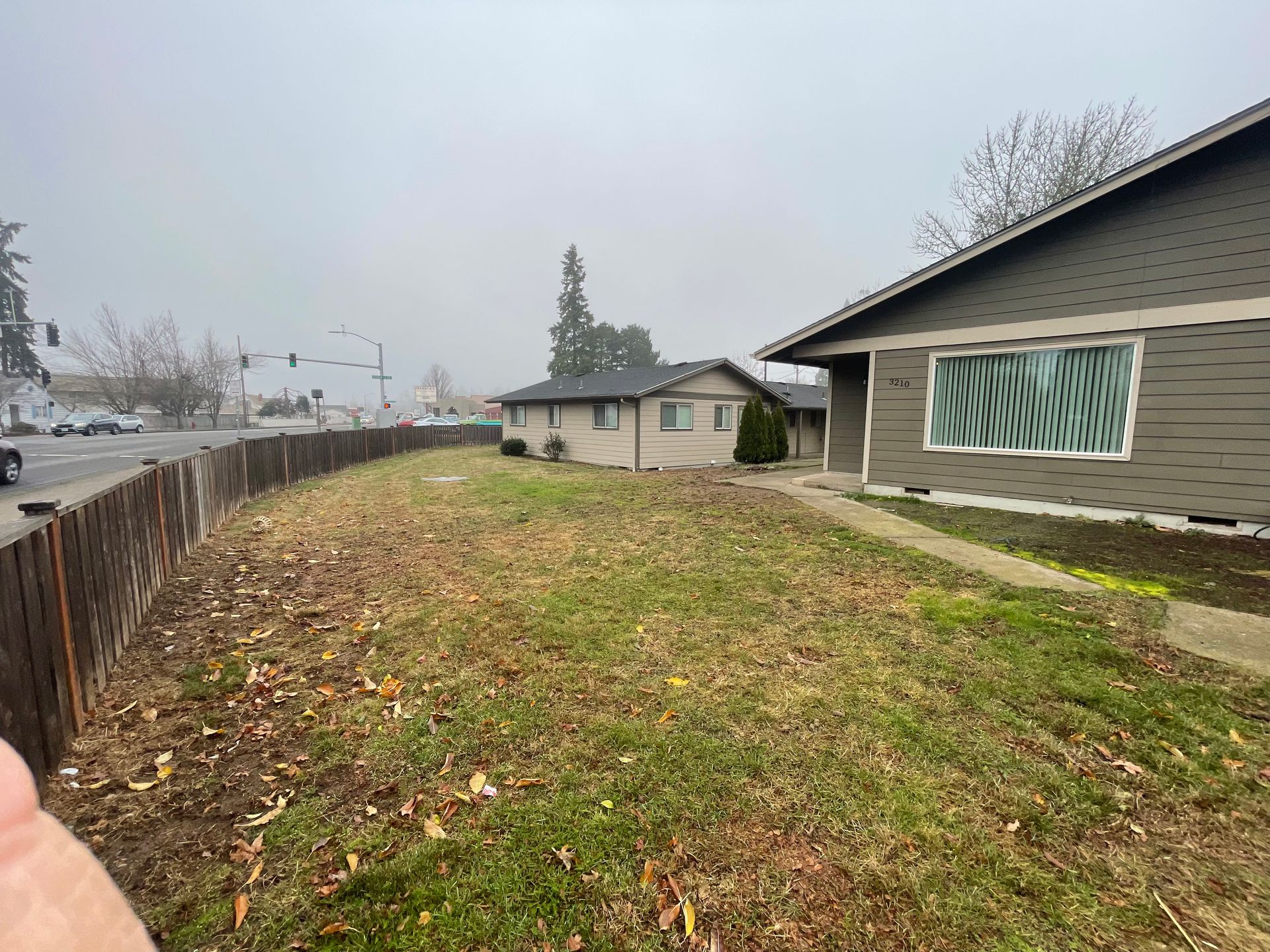 A person is standing in front of a house with a fence in the background.