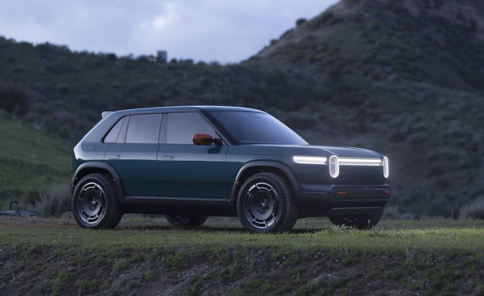 Dark green SUV with illuminated headlights parked on a grassy hill at dusk.