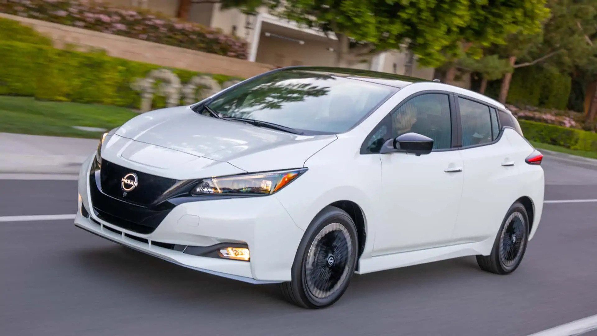 White Nissan sedan driving on a suburban street with trees and houses in the background