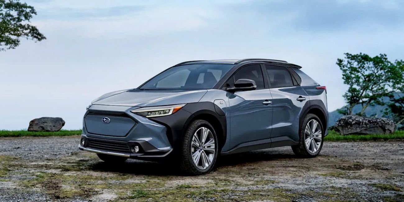 Blue-gray SUV parked on a rocky overlook with ocean and cloudy sky in the background