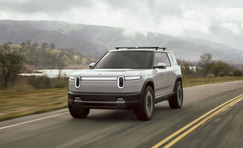 Silver electric SUV driving on a wet rural road with mountains in the background