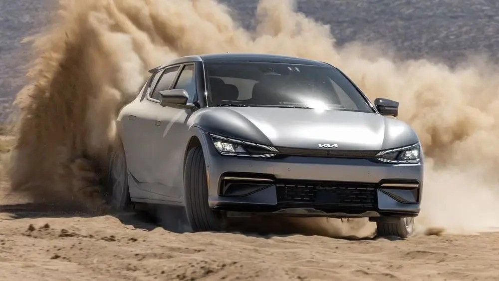 Silver car drifting through sand, kicking up a large dust cloud in a desert.