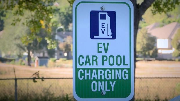 Blue and white sign reading “EV CAR POOL CHARGING ONLY” in a parking area