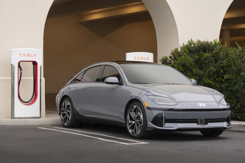 Gray electric sedan parked beside a Tesla charging station under an arched building entrance