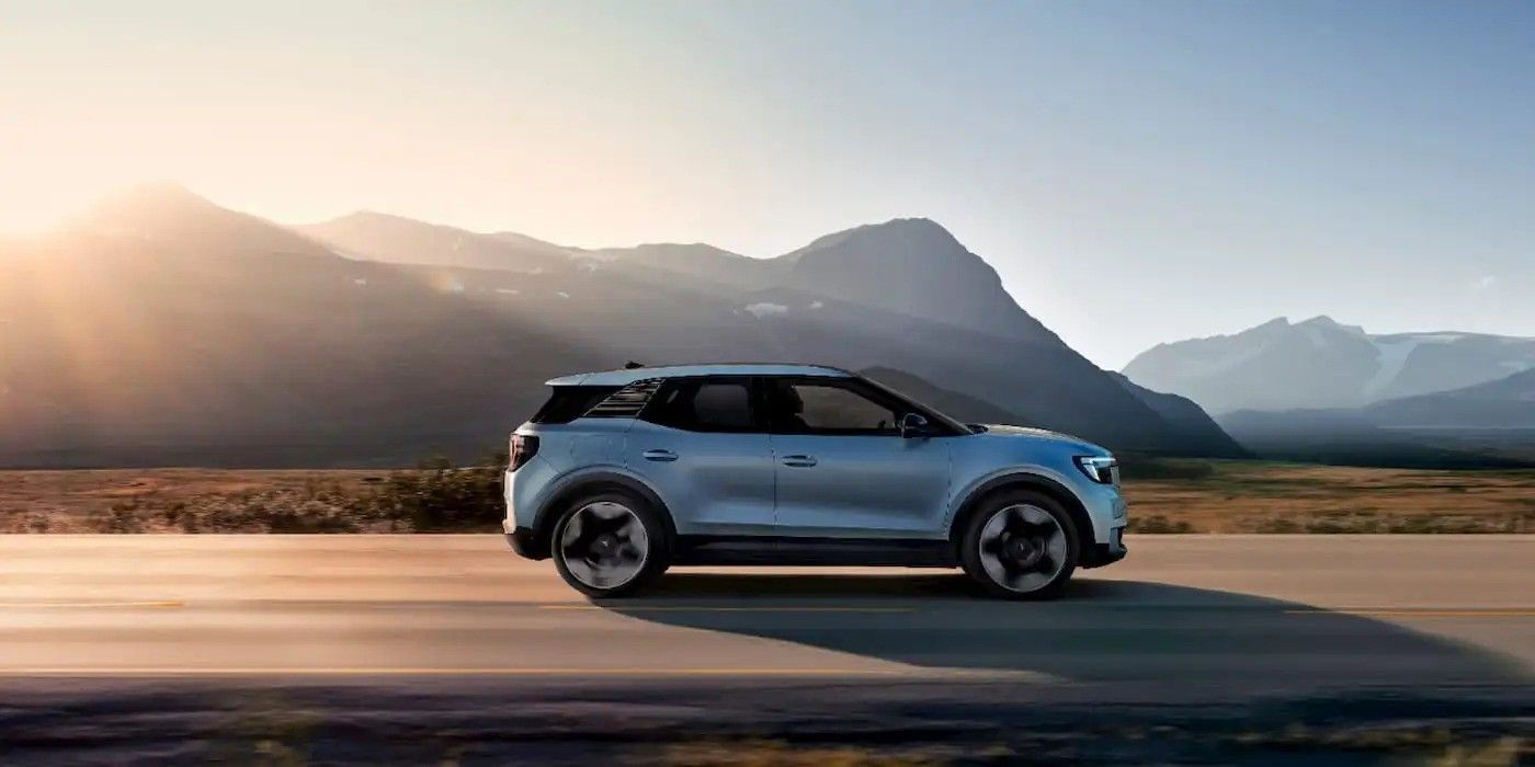 Silver SUV driving on a road with mountains and sunrise in the background