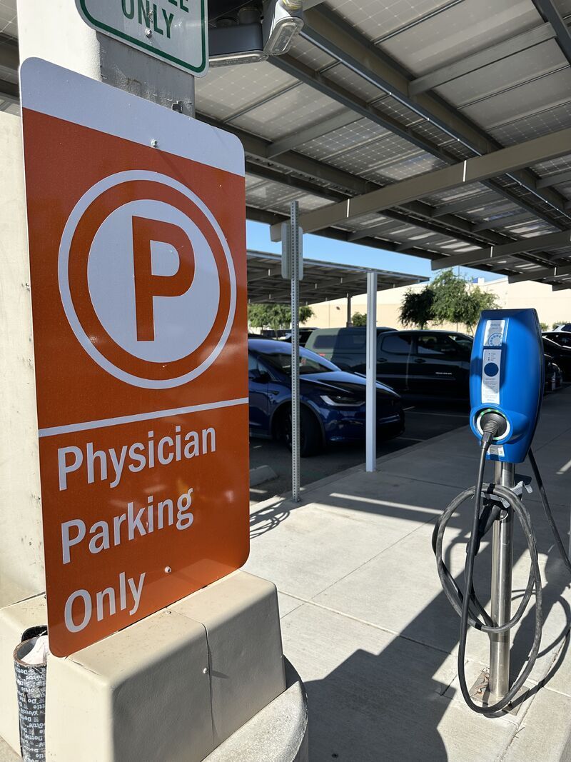 Orange “Physician Parking Only” sign beside a bike under a covered parking area.